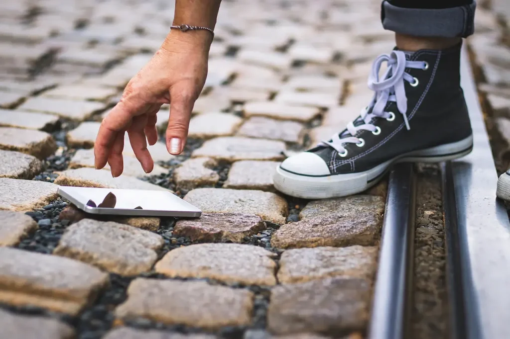 Person picking up a smartphone dropped on a cobblestone street near tram tracks