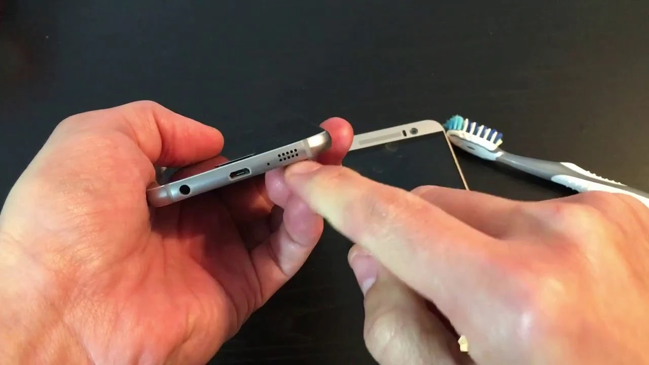 Person cleaning smartphone charging port with a small tool to remove dust and debris