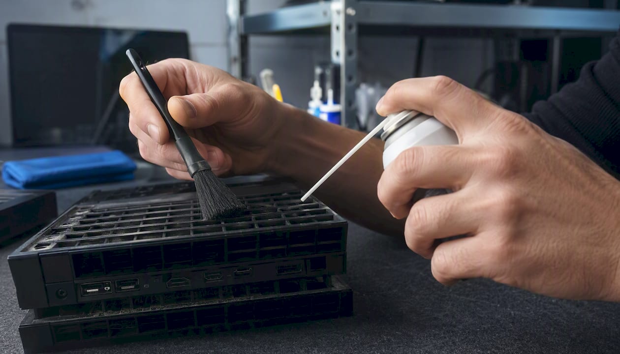 Hands cleaning dusty vents of a game console