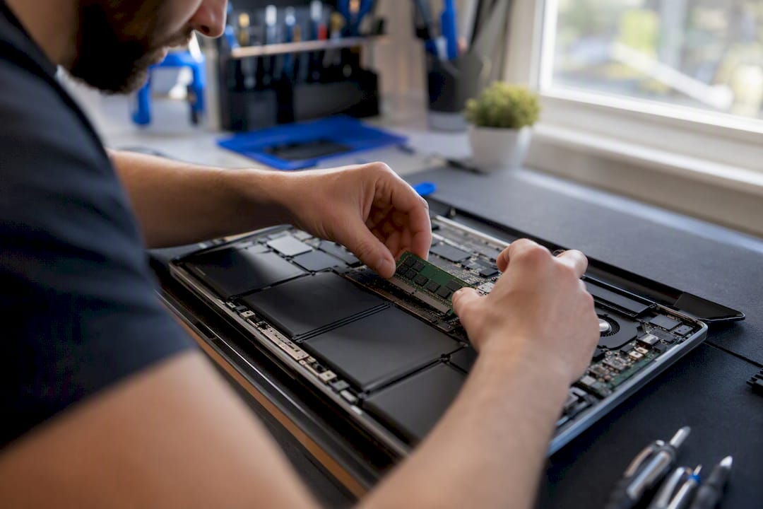 Hands inserting RAM stick into laptop motherboard